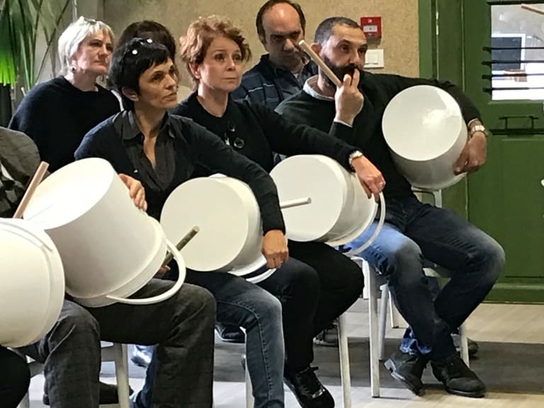 Partecipanti suonano grandi secchi bianchi con le bacchette